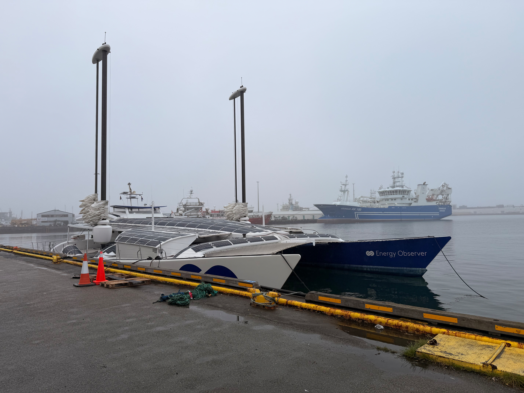 Two boats are docked at a harbor on a foggy day, with one of them named Energy Observer.